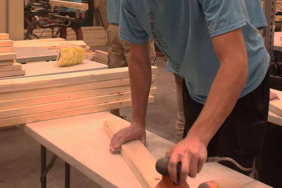 A student volunteer works with a sander and a piece of wood